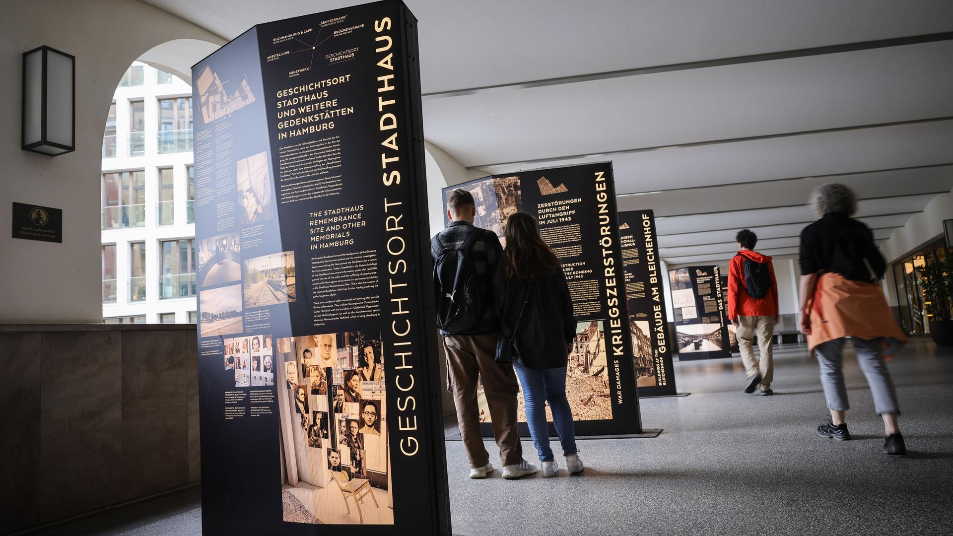 Im Hamburger Geschichtsort Stadthaus sollen die Fotos künftg zu sehen sein. Besucherinnen und Besucher stehen an Texttafeln in einem öffentlichen Durchgang.
       Im Hamburger Geschichtsort Stadthaus sollen die Fotos künftg zu sehen sein. Besucherinnen und Besucher stehen an Texttafeln in einem öffentlichen Durchgang.