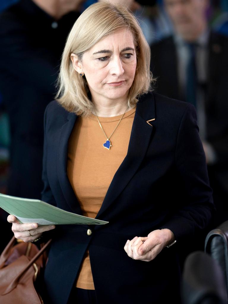 Eine Frau mit blonden Haaren und schwarzem Sakko hält eine Mappe in der Hand