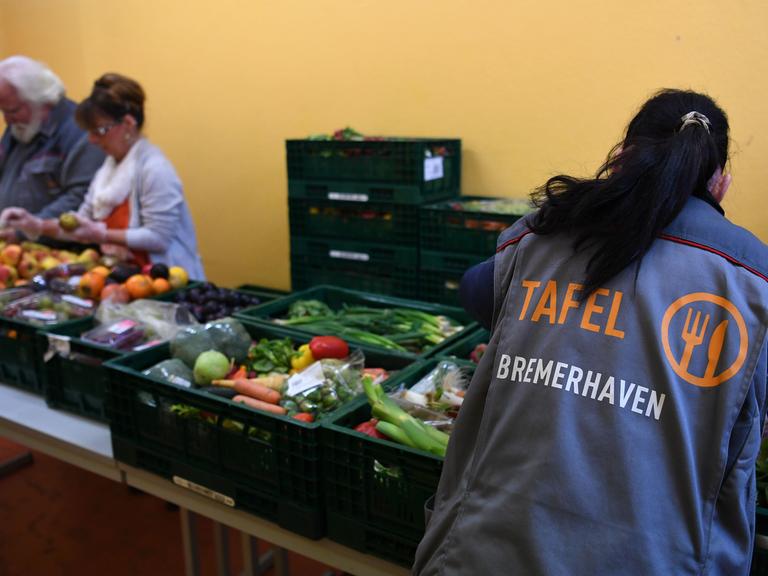 Eine Mitarbeiterin der Bremerhavener Tafel bereitet Obst und Gemüse zur Verteilung vor. Im Hintergrund sind zwei weitere Mitarbeitende zu sehen. Eine Mitarbeiterin der Bremerhavener Tafel bereitet Obst und Gemüse zur Verteilung vor. Im Hintergrund sind zwei weitere Mitarbeitende zu sehen.