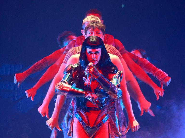 Katy Perry in einer Art Rüstung bei einem Konzert im August 2025, dahinter performen Tänzer