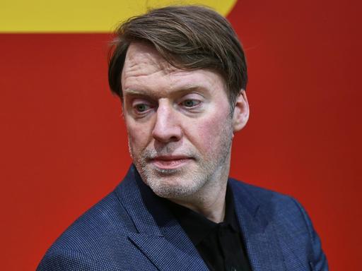 ZEIT-Journalist und Autor David Hugendick ernst blickend vor rotem Hintergrund.