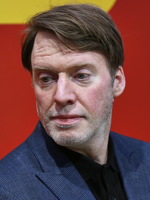 ZEIT-Journalist und Autor David Hugendick ernst blickend vor rotem Hintergrund.