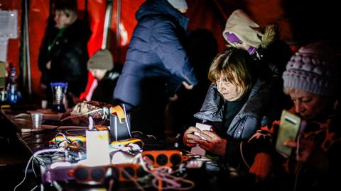 Menschen sitzen in einem Zelt, wärmen sich auf und laden ihre Handys auf.