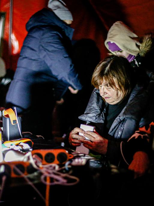 Menschen sitzen in einem Zelt, wärmen sich auf und laden ihre Handys auf.