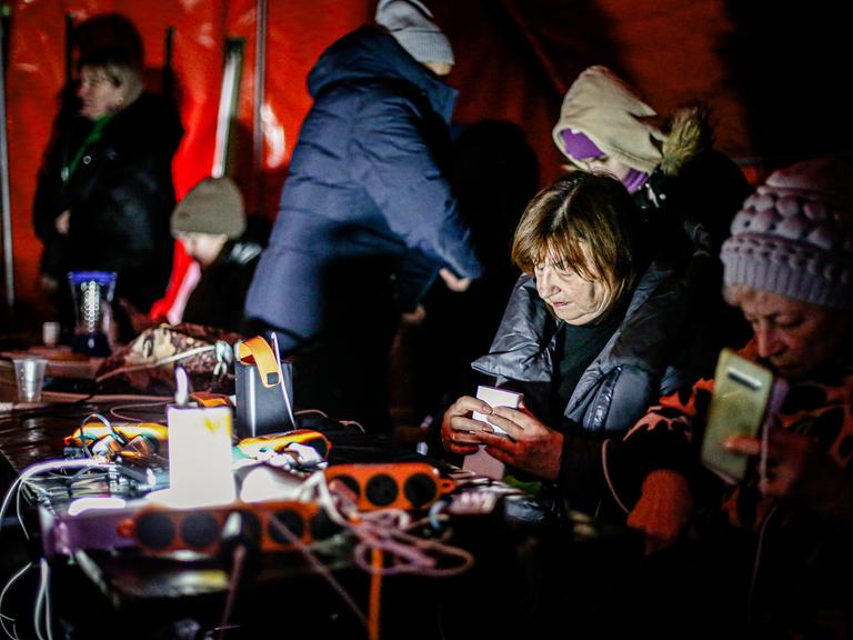 Menschen sitzen in einem Zelt, wärmen sich auf und laden ihre Handys auf.