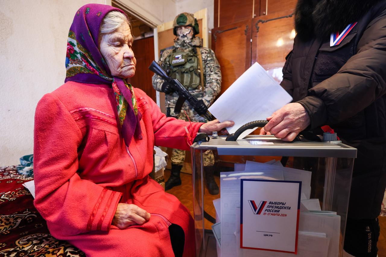 Sjewjerodonezk: Vorgezogene Wahl in den von Russland besetzten Gebieten in der Ukraine. Eine alte Frau steckt einen Wahlzettel in eine Wahlurne. Im Hintergrund steht ein Soldat mit Gewehr.