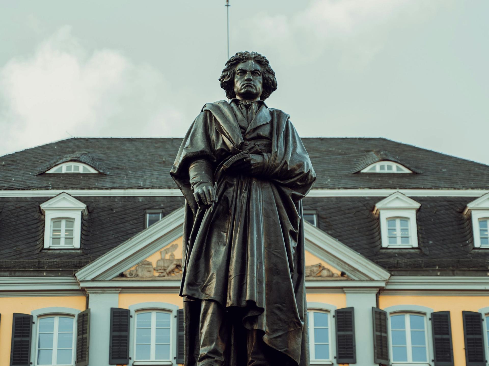 Blick auf die große Beethoven-Standfigur in Bonn, die den Komponisten mit wildem Haar und Falten werfenden Mantel zeigt.
