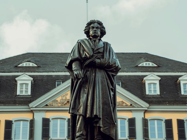 Blick auf die große Beethoven-Standfigur in Bonn, die den Komponisten mit wildem Haar und Falten werfenden Mantel zeigt.