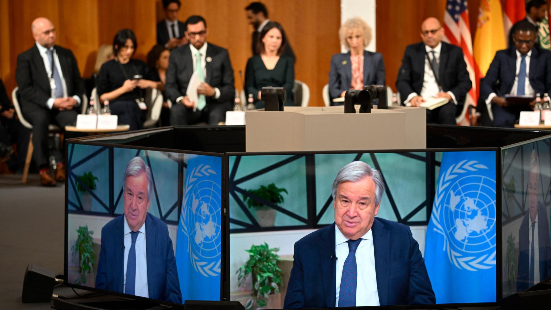 UNO-Generalsekretär Guterres ist auf dem Petersberger Klimadialog auf Bildschirmen zu sehen. Dahinter sitzen im Halbkreis weitere Teilnehmer.