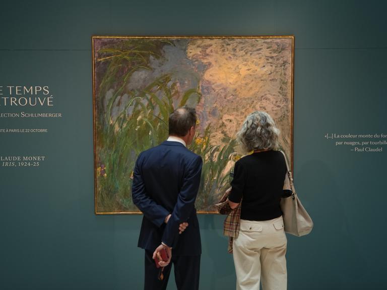 Zwei Personen stehen vor dem Gemälde „Iris“ von Claude Monet im Auktionshaus Sotheby’s in Paris.