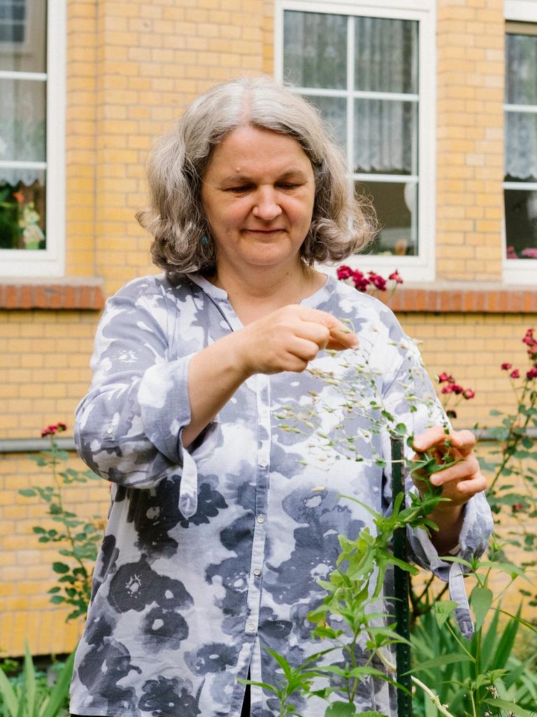 Gartentherapeutin Marlit Bromm steht vor einer Hauswand mit Fenstern und arbeitet an einem Hochbeet. Dabei zupft sie an einer Pflanze.