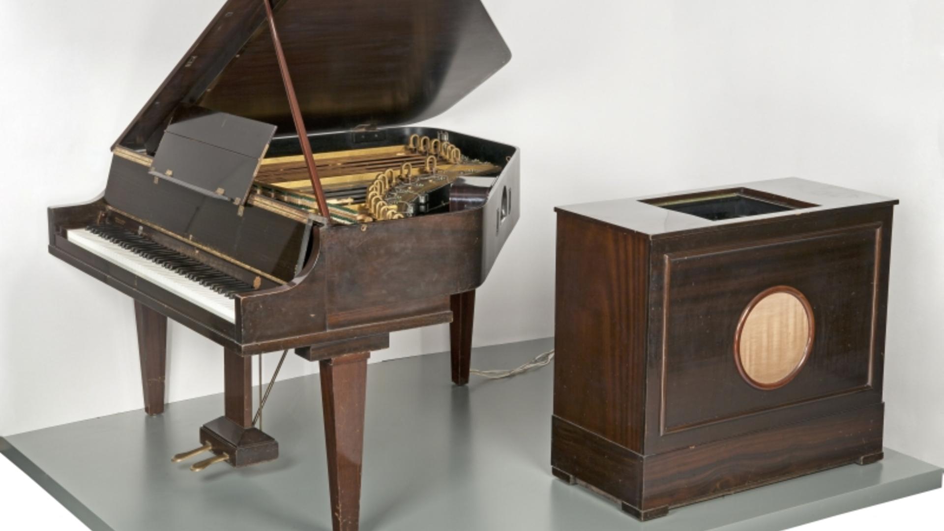 Blick auf einen holzfarbenen Flügel, der mit einer großen Lautsprecher-Box mit Drähten verbunden ist.