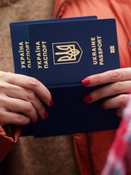 Zu sehen sind die Hände einer Frau, die einen ukrainischen Reisepass in den Händen hält. 