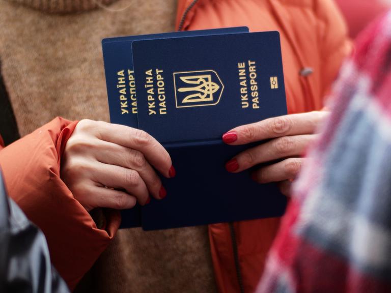 Zu sehen sind die Hände einer Frau, die einen ukrainischen Reisepass in den Händen hält. 