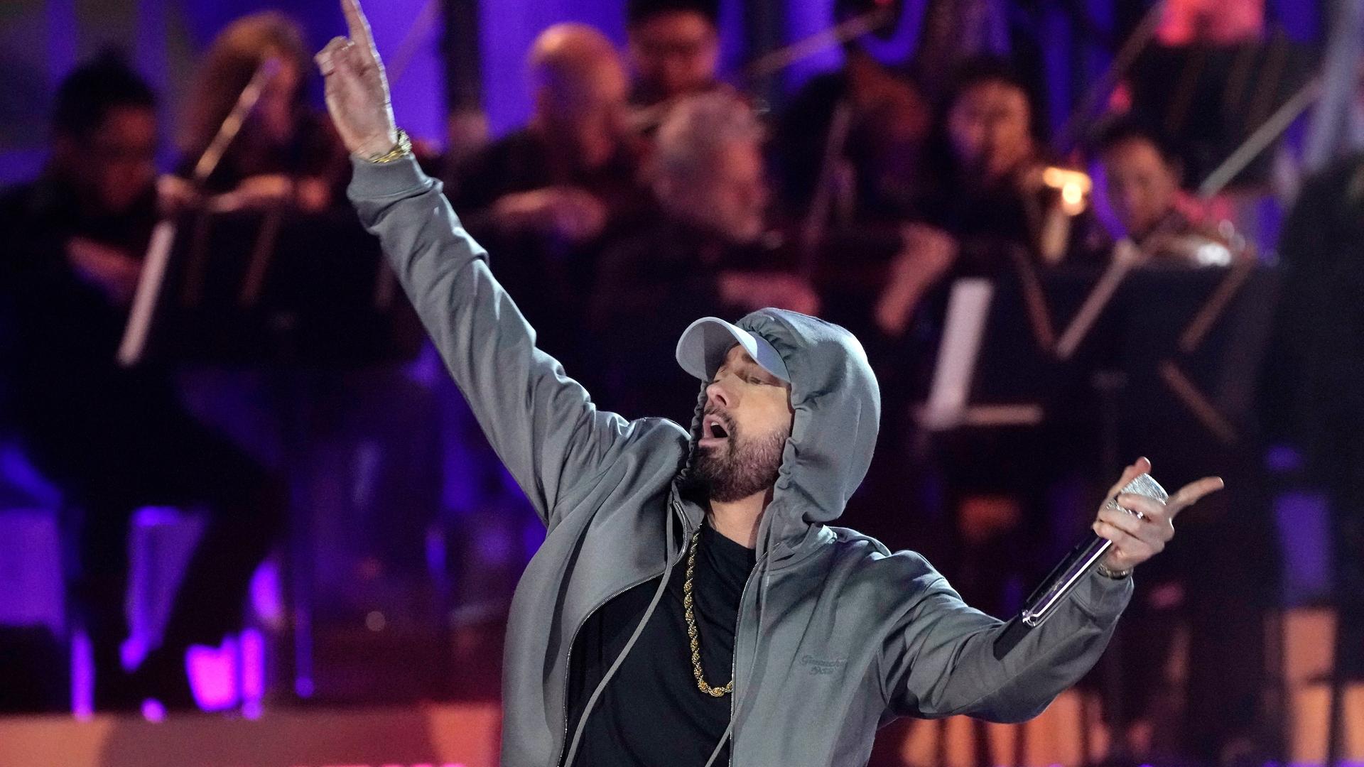 Ein Mann steht auf einer Bühne. Er hebt seine rechten Arm nach oben. Er trägt einen grauen Kapuzenpullover. der Sänger ist der US-Hiphoper Eminem.