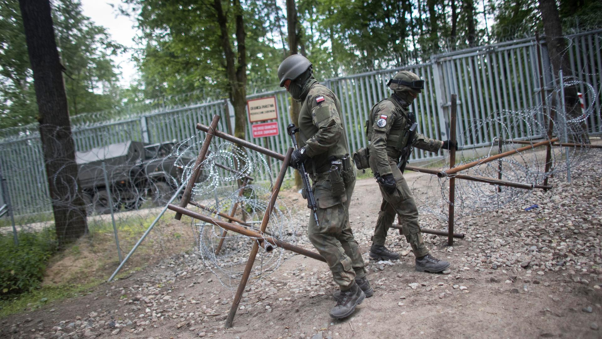 Grenze zwischen Polen und Belarus: Zwei polnische Grenzschützer drapieren Stacheldraht vor einem hohen Zaun.