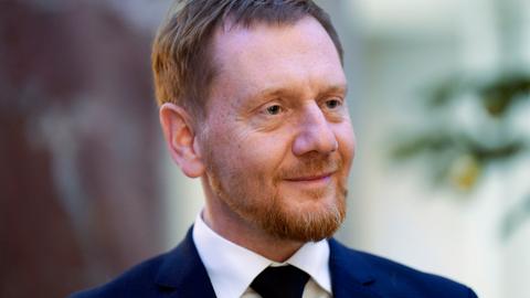 Der sächsische Ministerpräsident Michael Kretschmer trägt ein weißes Hemd, Krawatte und ein blaues Sakko und schaut an der Kamera vorbei.