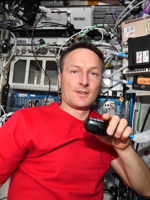 Matthias Maurer inmitten von Technik mit einem Mikron an der Hand an Bord der ISS