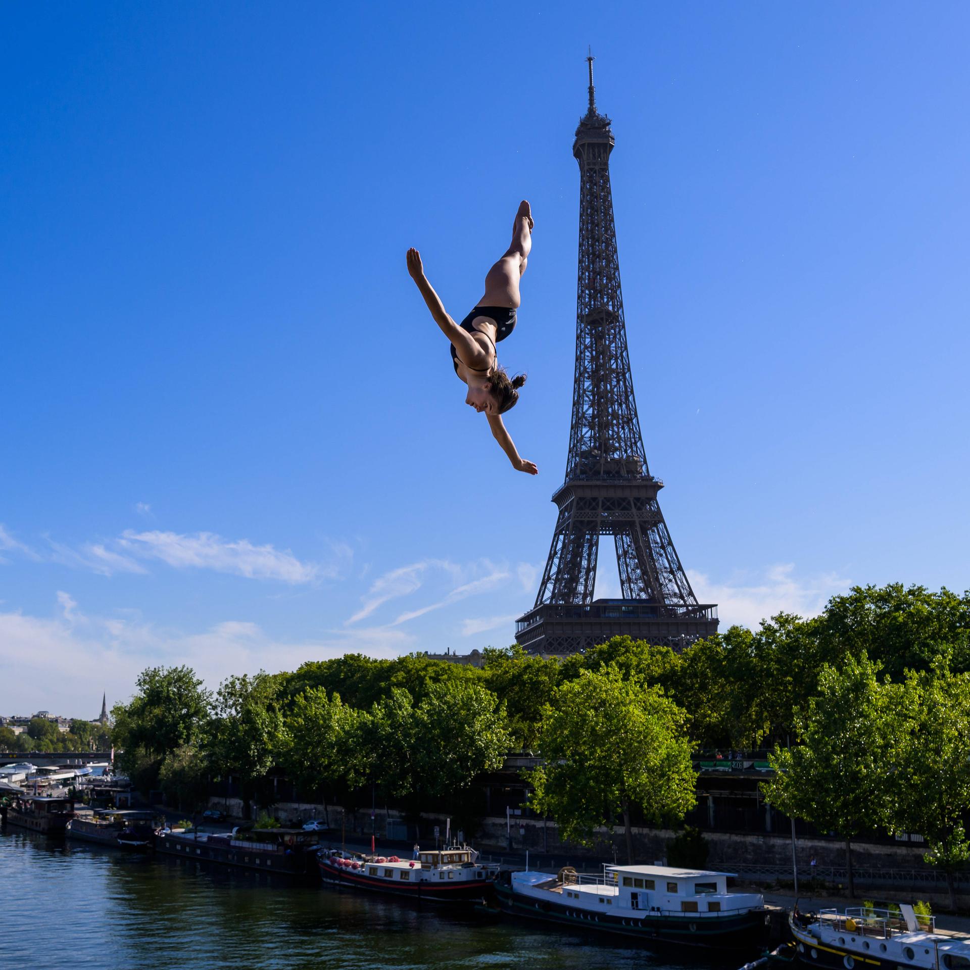 Maike Elena Halbisch beim Sprung von der 20-Meter-Plattform in Paris am 7.8.2026; sie fliegt durch die Luft - unter ihr ist die Seine und hinter ihr der Eiffelturm zu sehen.
