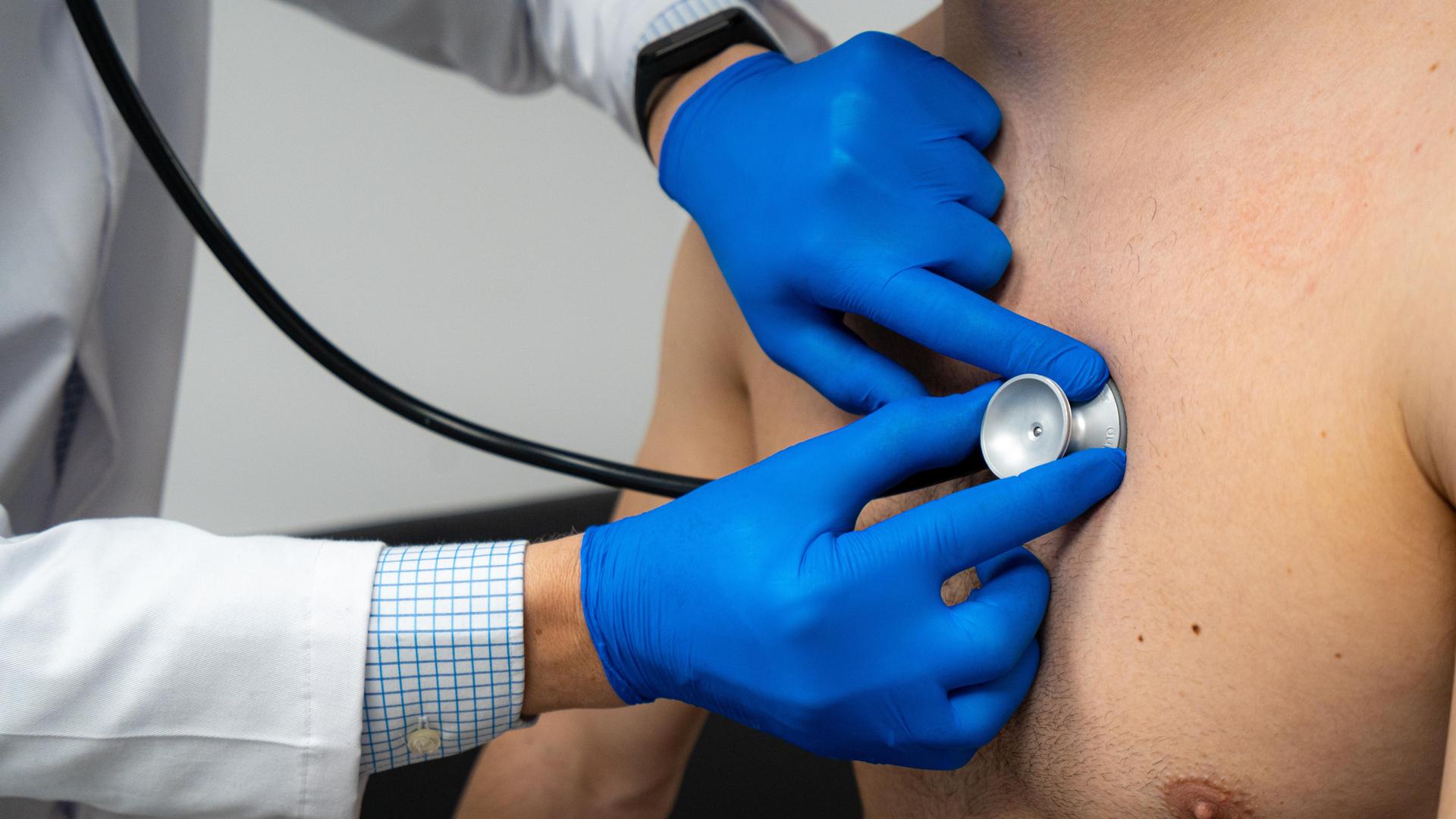 Ein Arzt untersucht das Herz eines Mannes mit einem Stethoskop. Er hört das Herz auf eine Herzschwäche ab. 