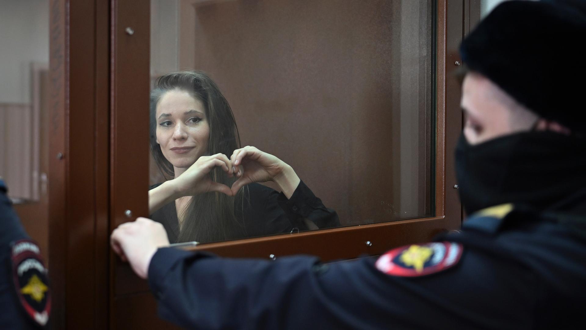 Eine Journalistin steht hinter Sicherheitsglas in einem Gerichtssaal in Moskau. Sie formt mit ihren Händen ein Herz. Eine Journalistin steht hinter Sicherheitsglas in einem Gerichtssaal in Moskau. Sie formt mit ihren Händen ein Herz.