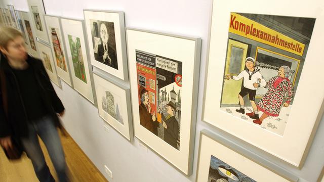 Eine Besucherin blickt im Wilhelm-Busch-Museum in Hannover auf Karikaturen, die an einer Wand hängen. Die Arbeiten gehören zu 391 ausgestellten Karikaturen, die von Zeichnerinnen und Zeichnern aus dem Umfeld der Satirezeitschrift "Eulenspiegel" stammen. 