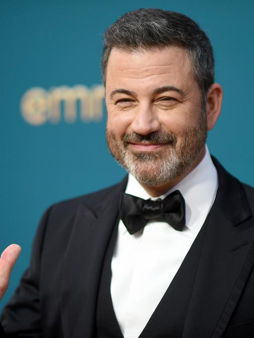 Late-Show-Moderator Jimmy Kimmel, ein Mann im mittleren Alter mit kurzen braunen Haaren im eleganten Anzug, winkt vor einer Wand, auf der Emmy Awards und NBC zu lesen ist. 12.09.2022