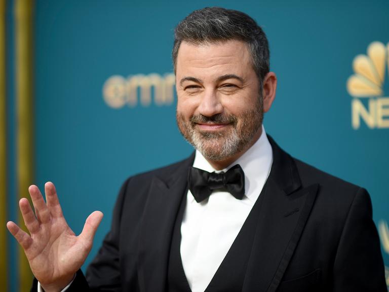 Late-Show-Moderator Jimmy Kimmel, ein Mann im mittleren Alter mit kurzen braunen Haaren im eleganten Anzug, winkt vor einer Wand, auf der Emmy Awards und NBC zu lesen ist. 12.09.2022