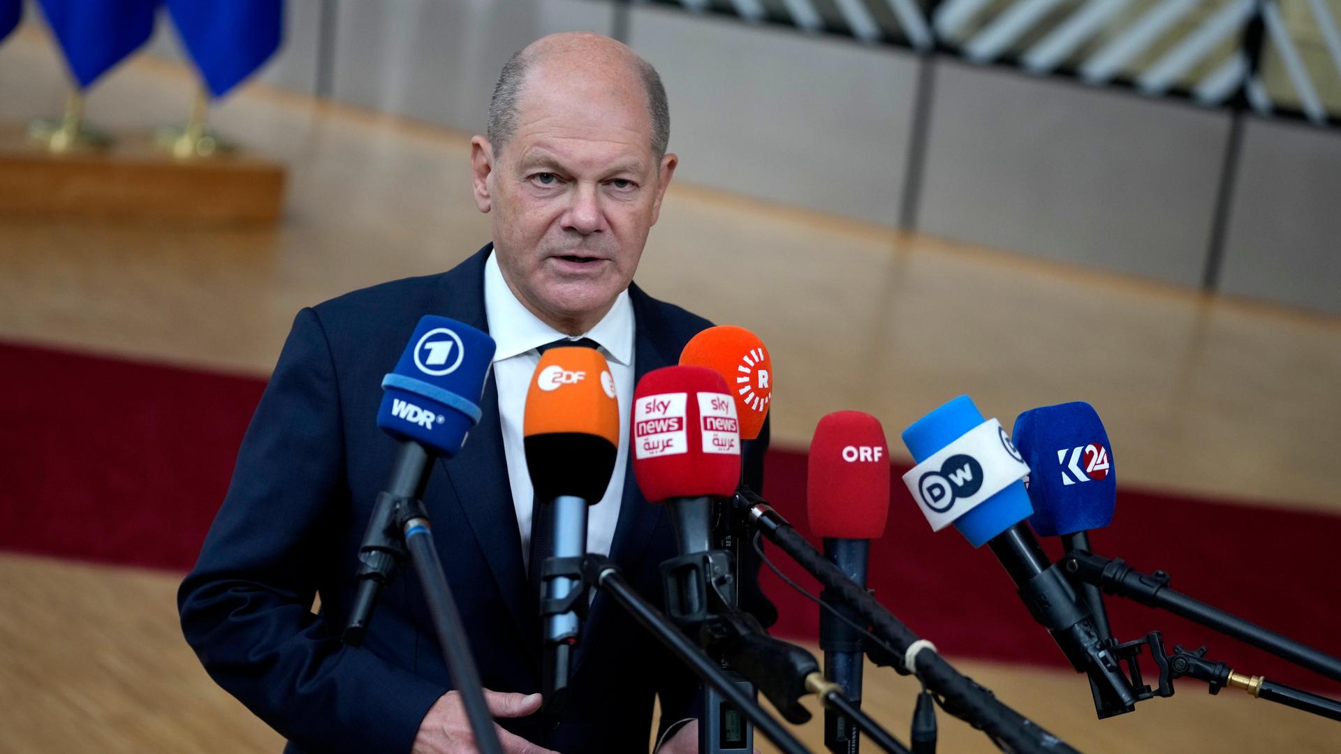 Das Foto zeigt den deutschen Bundeskanzler Olaf Scholz. Er spricht in verschiedene Mikrofone.