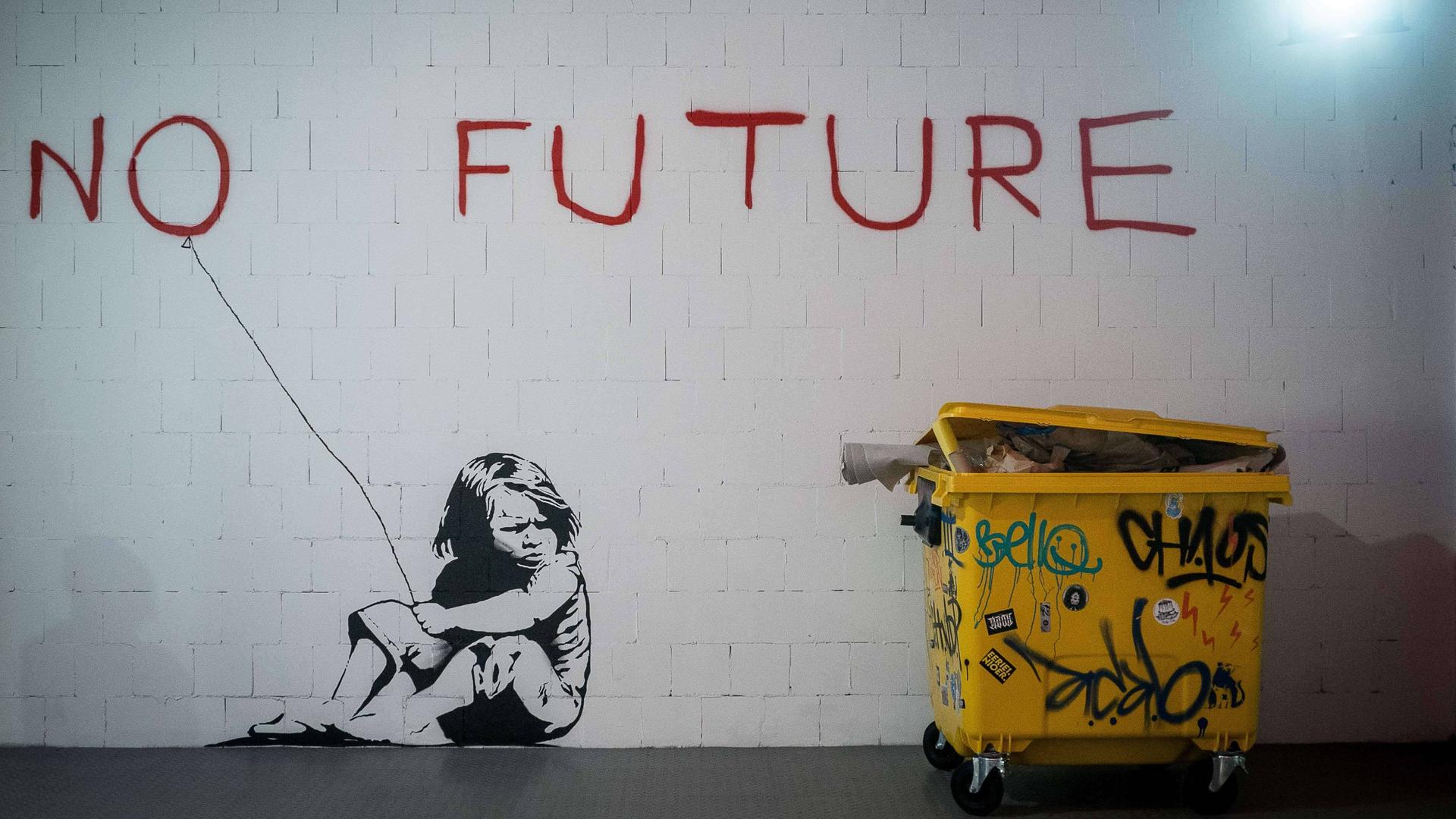 Ein großes Wandgraffiti zeigt den roten Schriftzug „no future“ und ein Mädchen, das daneben auf dem Boden kauert und das "o" wie einen Luftballon an einer Schnur hält. 