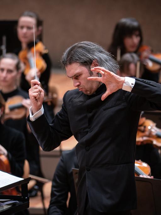 Der Dirigent Vladimir Jurowski steht mit offenen Haaren und kraftvoller Geste vor seinem Orchester.