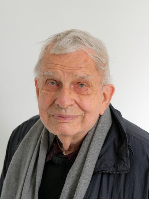 Der 84 Jahre alte Tomas Venclova schaut in die Kamera. Er hat weiße Haare, trägt eine dunkle Jacke und hat ein hellgraues Tuch um den Hals gelegt.