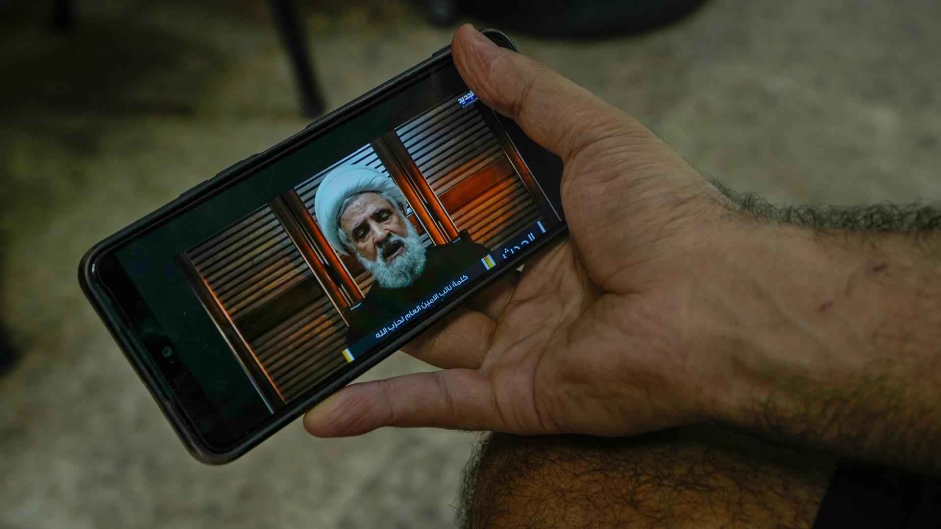 Ein Mann hält ein Smartphone in der Hand, auf dem das Programm von "Al-Manar TV" läuft