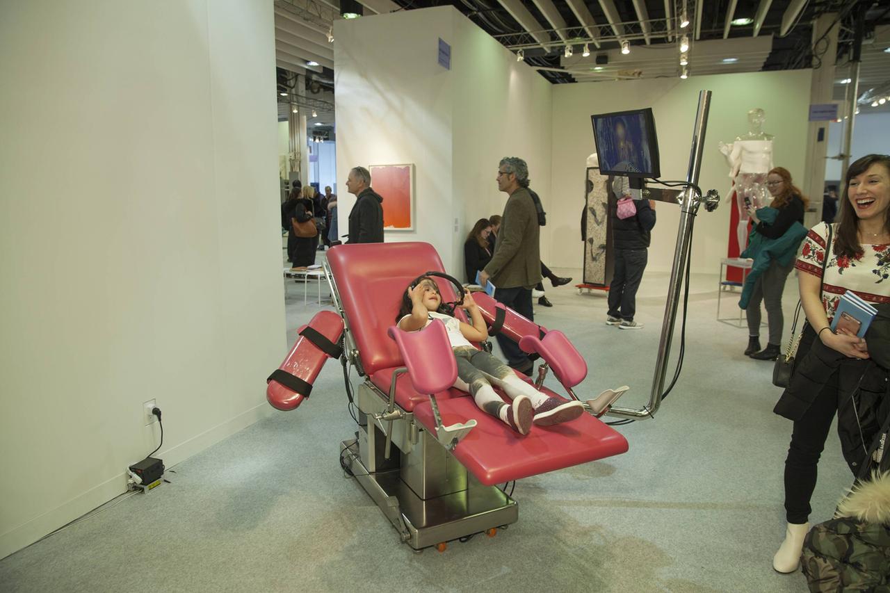 Ein pinker Untersuchungsstuhl steht in einem Ausstellungsraum mit Besucherinnen und Besuchern: Eine Arbeit von Tabita Rezaire bei einer Ausstellung in New York 2018.