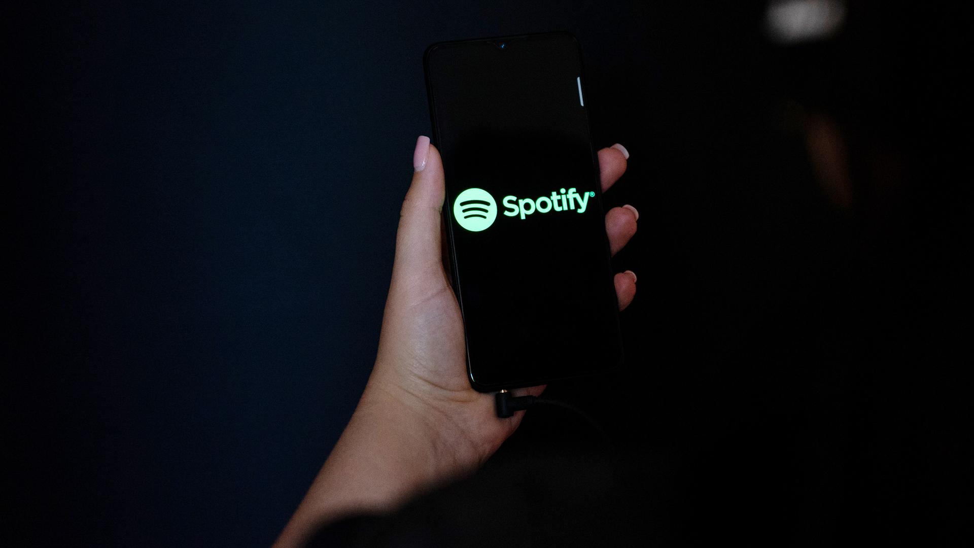 Eine Hand hält ein Smartphone mit dem Spotify Logo auf dem Display.