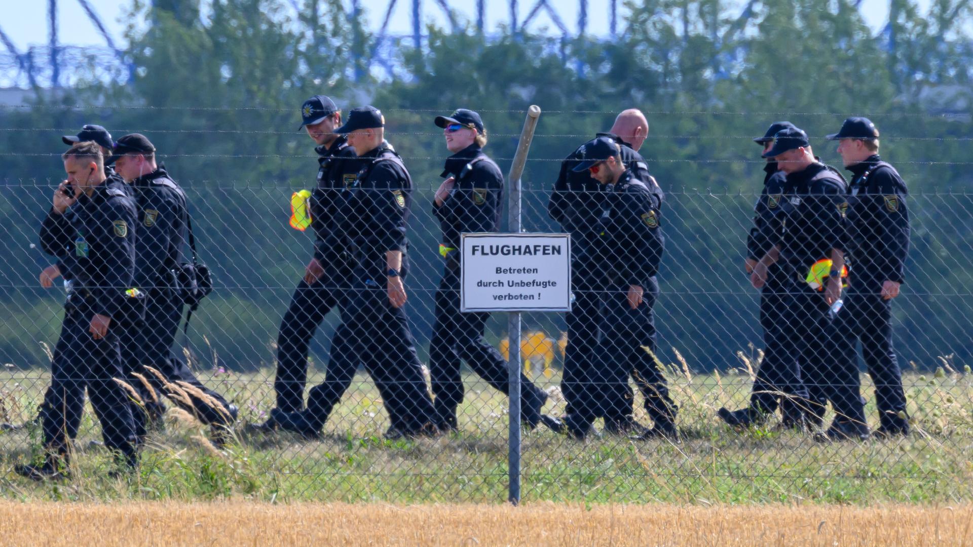 Einsatzkräfte der Polizei durchsuchen das Gelände abseits der Landebahn Nord auf dem Gelände des Flughafens Leipzig/Halle. Männer in Polizeiuniform hinter einem Gitterzaun. 