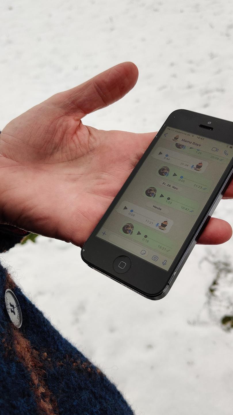 Eine Hand hält ein Smartphone auf der man einen Whatsapp-Chat sehen kann. DIe Person steht auf einer verschneiten Wiese.