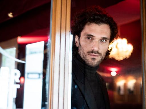 Sänger Vladimir Korneev schaut aus einem Fenster in der Bar jeder Vernunft in Berlin, im Hintergrund sieht man verschwommen einen Kronleuchter.