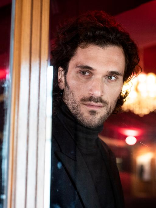 Sänger Vladimir Korneev schaut aus einem Fenster in der Bar jeder Vernunft in Berlin, im Hintergrund sieht man verschwommen einen Kronleuchter.