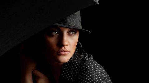 Bild in Schwarztönen: Elegante Frau mit Hut und Schirm im Stil der 1930er Jahre in Chicago, mysteriöser Blick.