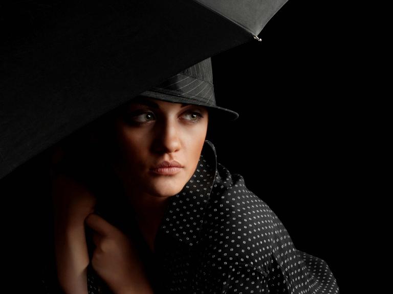 Bild in Schwarztönen: Elegante Frau mit Hut und Schirm im Stil der 1930er Jahre in Chicago, mysteriöser Blick.