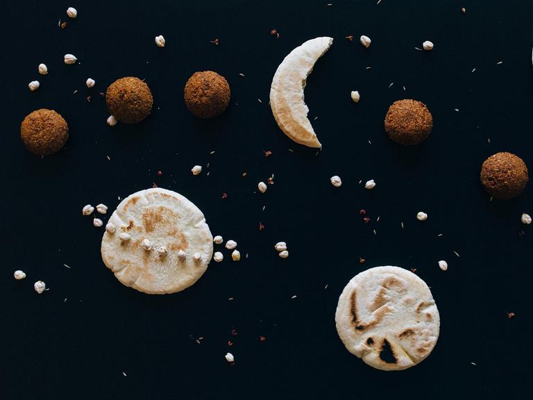 Auf einem dunklen Untergrund liegen diverse Kekse und Nüsse, die den Weltraum mit Monden und Planeten darstellen.