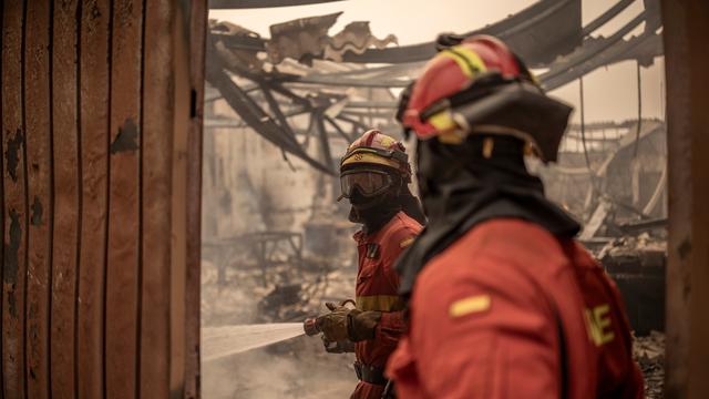 Feuerwehrleute stehen in einer verbrannten Umgebung.