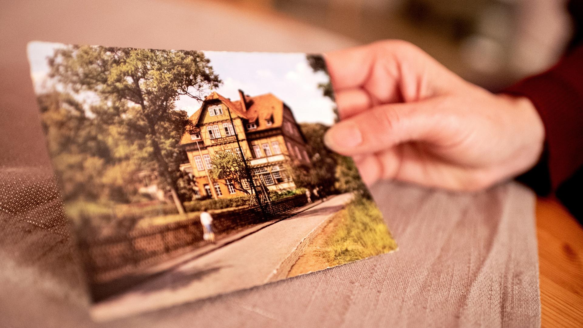 Eine Frauenhand hält eine historische Postkarte der Kinderheilanstalt Bad Salzdetfurth.  