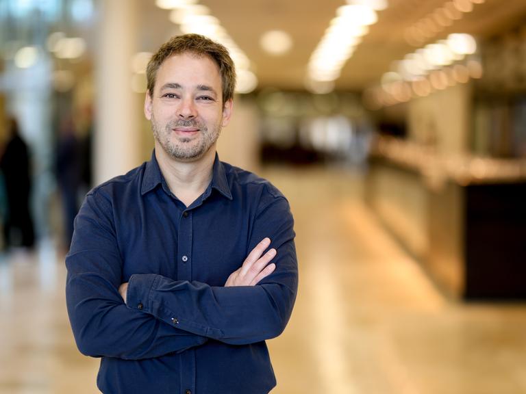 Ein Mann mit blauem Hemd und kurzen dunklen Haaren steht mit verschränkten Armen im Foyer eines Konzerthauses