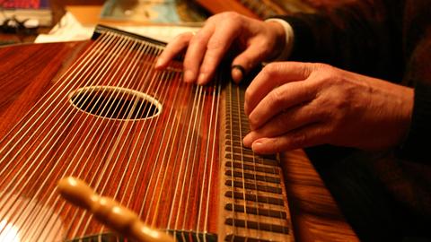 Blick auf zwei Hände, die kundig eine Zither deutscher Bauart spielen.