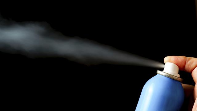 Finger, der Dampf aus einer blauen Spraydose auf einen schwarzen Hintergrund sprüht, wodurch ein rauchiger Effekt entsteht