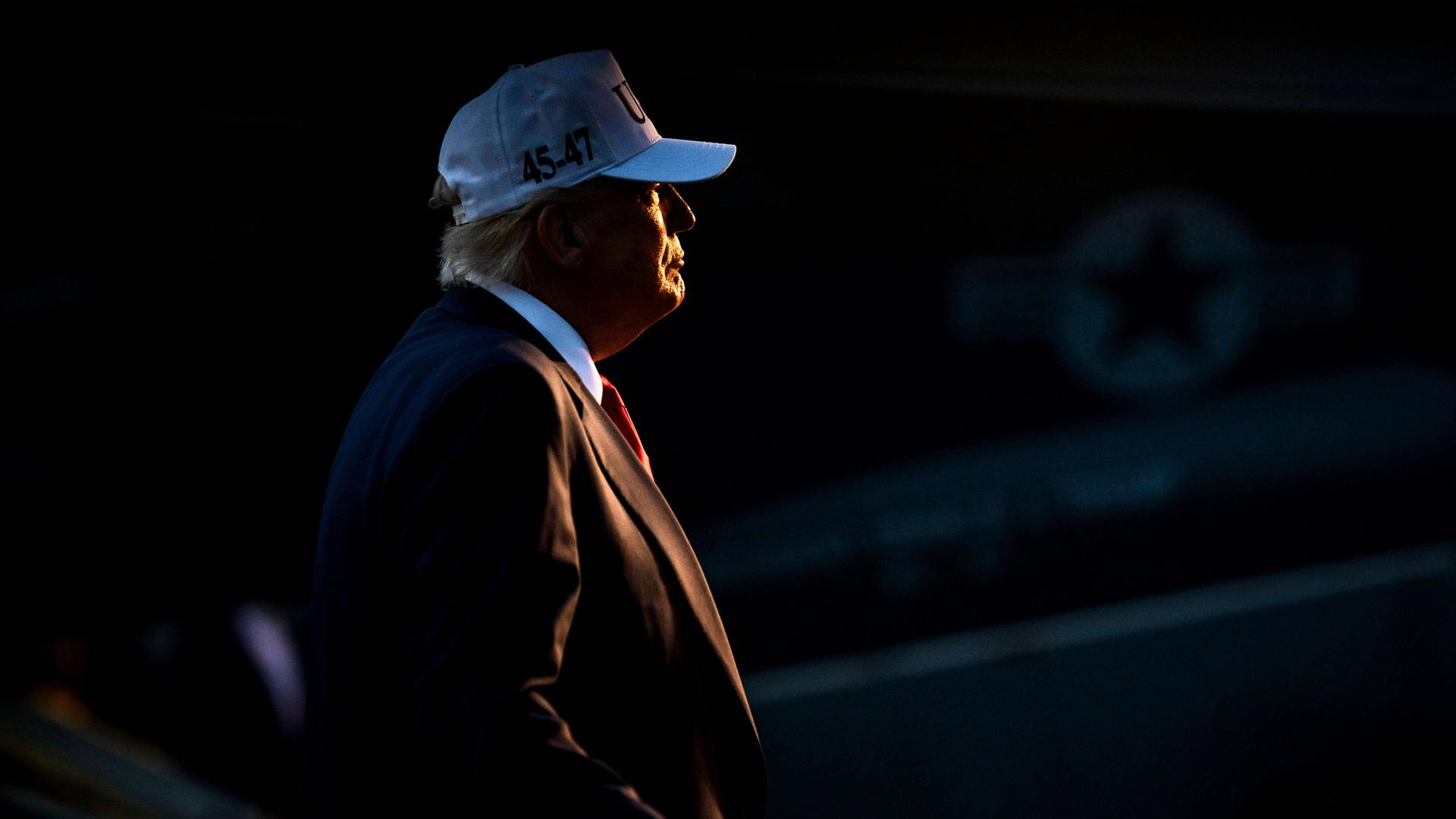 Trump bei Nacht im Scheinwerfer, mit roter Krawatte und weißer Baseballmütze Trump bei Nacht im Scheinwerfer, mit roter Krawatte und weißer Baseballmütze