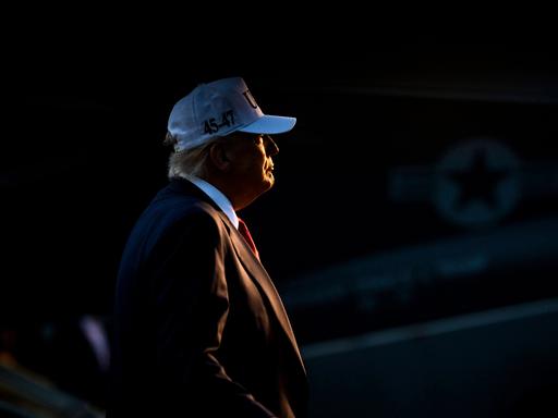 Trump bei Nacht im Scheinwerfer, mit roter Krawatte und weißer Baseballmütze Trump bei Nacht im Scheinwerfer, mit roter Krawatte und weißer Baseballmütze