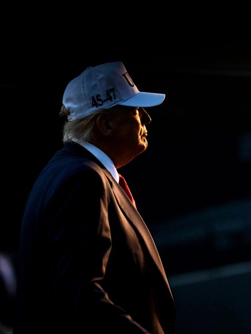 Trump bei Nacht im Scheinwerfer, mit roter Krawatte und weißer Baseballmütze Trump bei Nacht im Scheinwerfer, mit roter Krawatte und weißer Baseballmütze